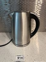 Front view of stainless steel Cuisinart kettle with black handle and power cord visible.