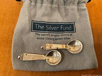 Two sterling silver salt spoons on branded grey pouch