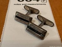 Top-down view of both cufflinks on paper, showing rectangular faces and T-bar toggles.