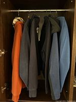 Five men's long sleeve jackets hanging in a closet, various colors including rust-orange, dark gray, black, olive green, and blue.