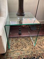 Front view of the clear glass end table beside sofa with lamp on top