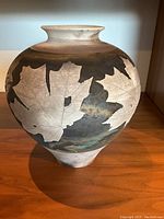 Front angled view of the pottery vase showing large maple leaf designs in white against dark brown background with mottled colors.
