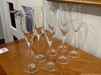 Eight clear Nachtmann champagne flutes arranged on a wooden table. View shows full set from the front.