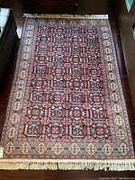 Full view of rectangular carpet with repeating geometric floral pattern and fringed ends