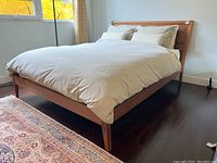 Full view of assembled teak bed frame with mattress and bedding