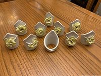 Set of 10 white ceramic napkin rings with yellow flower decoration arranged upright on wooden table, showing front flower detail on each.