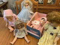 Photo showing five vintage dolls arranged on a wooden table, including a sleeping baby doll in original box, Cinderella doll, and others.