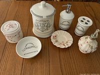Seven white ceramic bathroom accessories arranged on a wooden surface