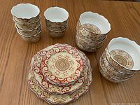 Stacked small and bigger bowls with red and gold mandala patterns on wooden table