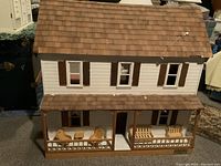 Front view of the wired wooden doll house showing roof, windows, porch, and porch furniture including chairs and benches.