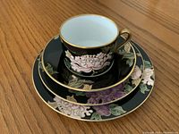 Porcelain cup stacked on saucer, small plate, and bead and butter plate showing floral design and gold accents.