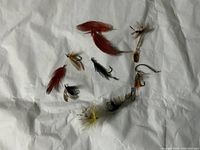 Image showing an assortment of fly fishing lures and flies laid out loosely on a white sheet, highlighting different styles and feather colors.