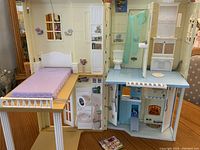 Interior view of fold-up dollhouse showing bedroom with bed, bathroom with shower and toilet, kitchen with stove and washing machine, and living area with fireplace.