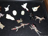 Top view of multiple small glass animal miniatures including bird, dog, lizard, and child figurines on black surface.