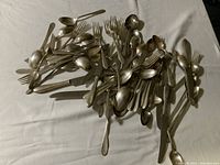Overall pile of assorted flatware including spoons, forks, knives, some pieces larger serving utensils.