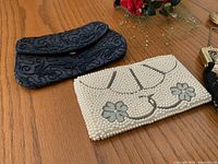 Black bead embroidered evening clutch and white pearl embellished clutch showing floral motifs on wood surface