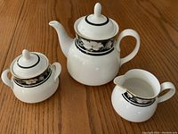 Photo showing the full tea set of three pieces: teapot, sugar bowl, cream jug with floral black decorative bands