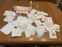 Top-down view of 22 vintage handkerchiefs arranged on wooden surface showing details of edges, embroidery, and fabric pouch.
