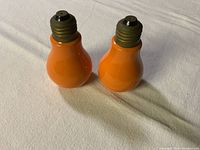 Front view of two orange light bulb shaped salt and pepper shakers with metal tops on white background.