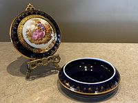Photo showing the cobalt blue and gold trinket box with lid displayed on a brass stand highlighting the detailed painting and gold accents.