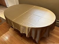 Tablecloth fully spread on an oval table showing golden metallic silky texture and fit.