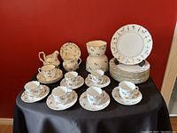 Complete view of the 29-piece Limoges luncheon set on black cloth against red background showing various cups, saucers, nesting bowls, cream and sugar container, and stacked dessert plates.