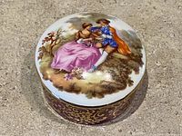 Top view of round porcelain trinket box with painted romantic couple scene on lid.