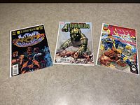 Three collectible comic books displayed side by side on a flat surface, clearly showing the front cover art and titles.