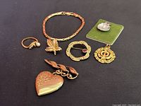 Seven mixed metal jewelry pieces arranged together on dark cloth showing bracelets, pins, pendant, ring, and brooch locket.