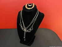 Four gold-tone necklaces displayed on black velvet bust, one with large loops, one with a delicate chain, and two with gemstone pendants.