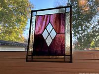 Photo of the stained glass panel showing the purple central diamond pattern against the sky with detached hanging chain visible on the side