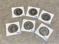 Six Canadian half dollar coins dated 1969, 1975, 1978, 1981, 1985, and 1986 in cardboard holders laid out on a surface.