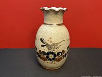 Front side view of Tonala pottery vase with bird and floral decoration on beige stoneware background.