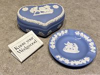 Heart-shaped blue and white Wedgwood trinket box with lid, ashtray, and informational booklet about Wedgwood visible.