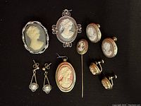Top view of all 10 vintage cameo jewelry pieces including pendants, earrings, brooch, and pins on black background.