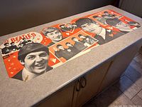 Full view of the 18.5 x 53 inch Beatles collage poster laid flat on a counter showing the entire artwork with color and portrait details.