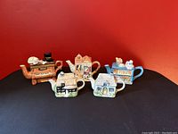 Front view of five vintage ceramic collector teapots on black surface with red background.