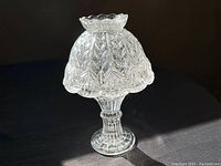 Vintage crystal pressed glass fairy light candle holder with bell-shaped lid and pedestal base, photographed against dark and red backgrounds.