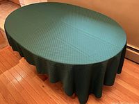 Table fully covered with the forest green tablecloth to show fit and overall appearance on an oval wooden table.