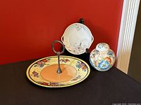 View of all three vintage serving dishes on counter against red wall showing the Nippon plate with metal handle, ginger jar, and Phoenix China plate.