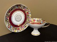 View of pedestal teacup and saucer showing pictorial scene and gilt accents
