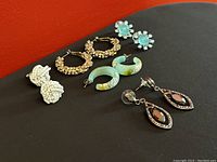 All five pairs of vintage pierced earrings laid out on a black surface, showing front view of each pair with varying metal tones and stones.