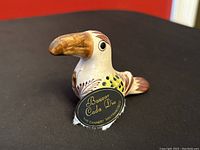 Profile front view of the Tonala ceramic bird figurine showing the Bazaar Cada Dia tag indicating origin.