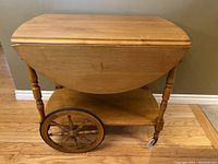 Image showing the folded wooden teacart with large spoked wheels and lower shelf on wooden floor.