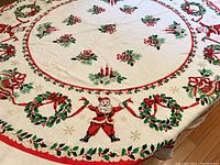 Full view of round vintage Christmas linen tablecloth laid out on a table showing central and border designs.