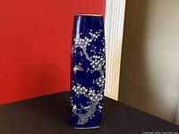Front and side view of the squared cobalt blue ceramic vase decorated with cherry blossoms and birds on a dark blue background with gold gilt rim
