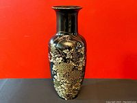 Front view of black porcelain vase with gold chrysanthemum and floral designs against red background