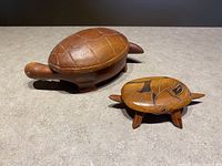 Two wooden turtle-shaped jewelry boxes on a light surface; one larger with textured shell and one smaller with carved decorative shell.