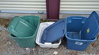 Three storage bins with lids, green, white, and blue, shown outdoors on gravel.
