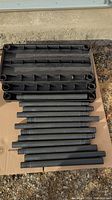 Black plastic shelving trays and tubular poles laid out on cardboard surface.